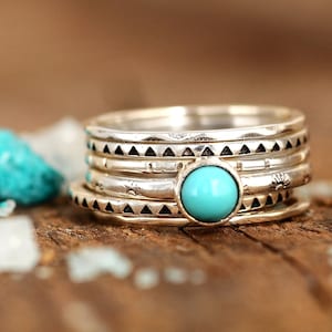 May include: A set of five silver rings featuring a turquoise gemstone. The rings are stacked on top of each other and have different designs.