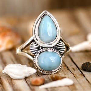 May include: A silver ring featuring two teardrop-shaped blue gemstones. The ring has a delicate design with intricate details.