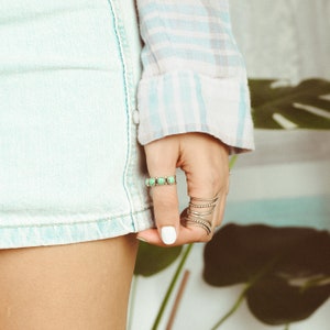 May include: A woman's hand wearing a silver ring with green stones and several thin silver rings.