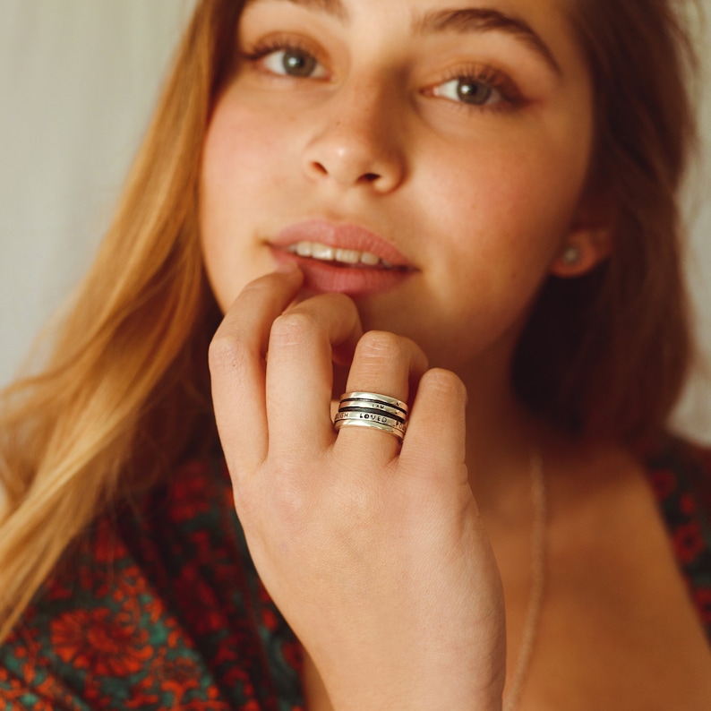 May include: A close-up of a person's hand wearing a silver ring with the words "LOVE", "GRATITUDE", and "FAITH" engraved on it.