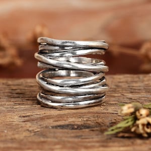May include: A silver ring with a unique design of multiple intertwined bands. The ring is made of a textured metal and has a rustic look.