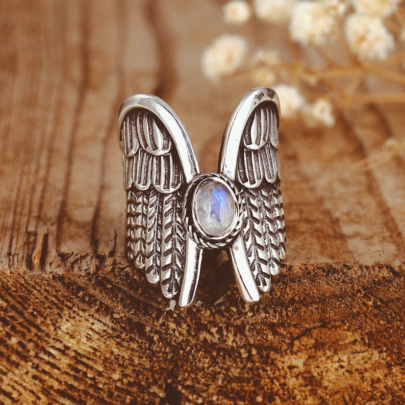 May include: Silver ring with a moonstone set in the center, shaped like two wings.