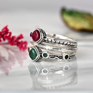 May include: A set of three silver rings with green and red gemstones. The rings are stacked on top of each other and have intricate designs.