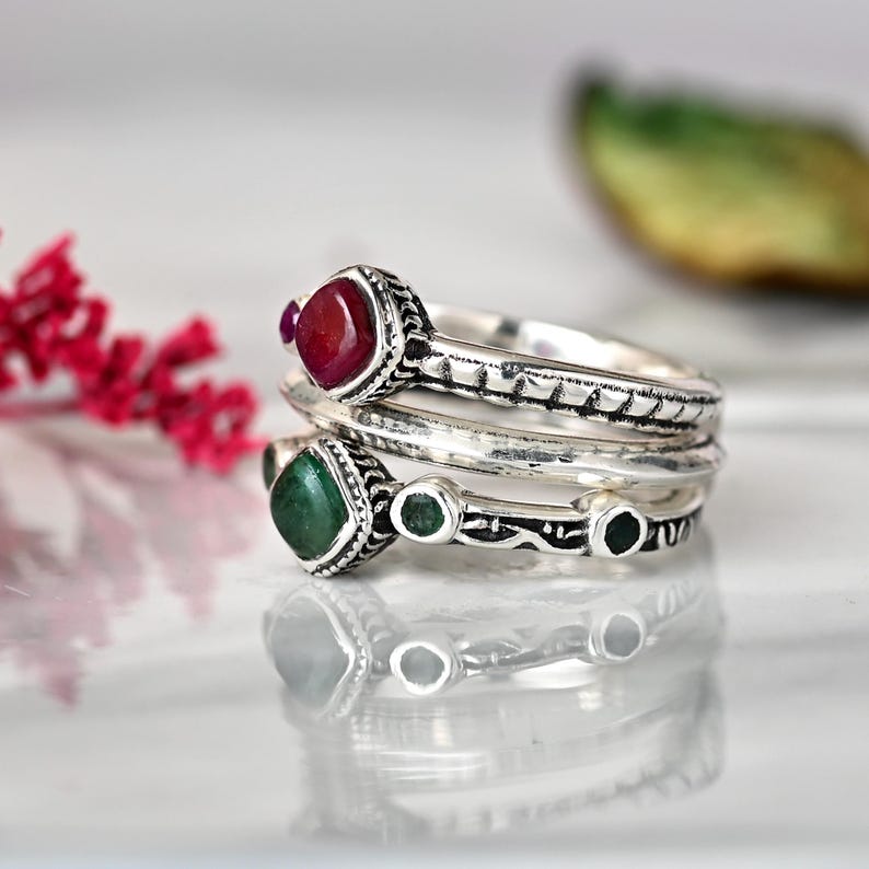 May include: A set of three silver rings with green and red gemstones. The rings are stacked on top of each other and have intricate designs.