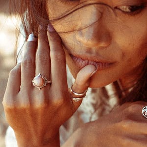 Op de afbeelding: Een zilveren ring met een zeshoekige roze edelsteen. De ring zit aan een vinger.