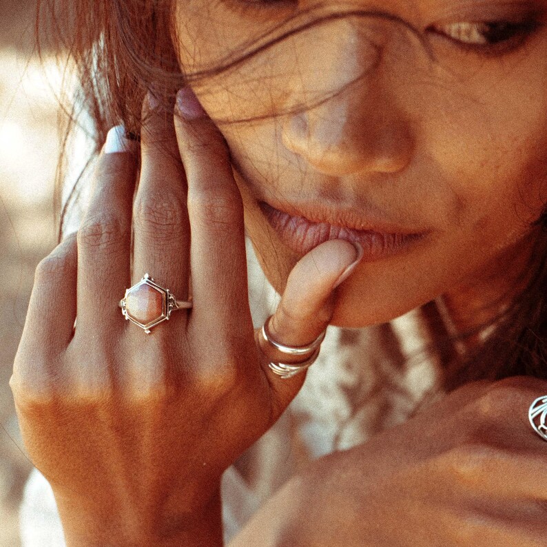 Op de afbeelding: Een zilveren ring met een zeshoekige roze edelsteen. De ring zit aan een vinger.