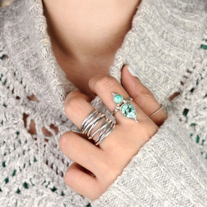 May include: A silver ring with two turquoise stones. The ring is worn on a finger with several other silver bands.