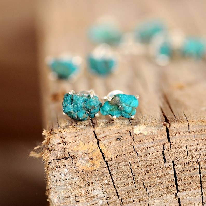 May include: A pair of silver earrings with turquoise stones. The stones are a deep blue-green colour and have a rough, natural texture.
