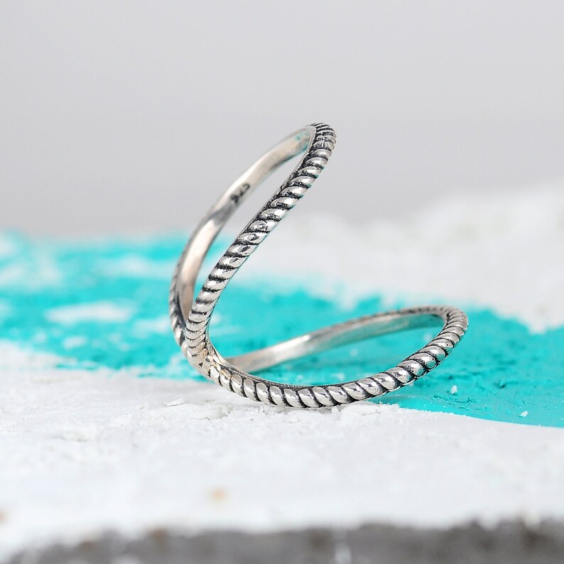 May include: A silver ring with a twisted rope design. The ring is open and can be worn on multiple fingers.