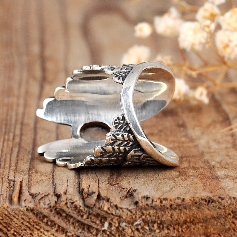 May include: Silver ring with a detailed design of a bird's wing. The ring is open and adjustable.