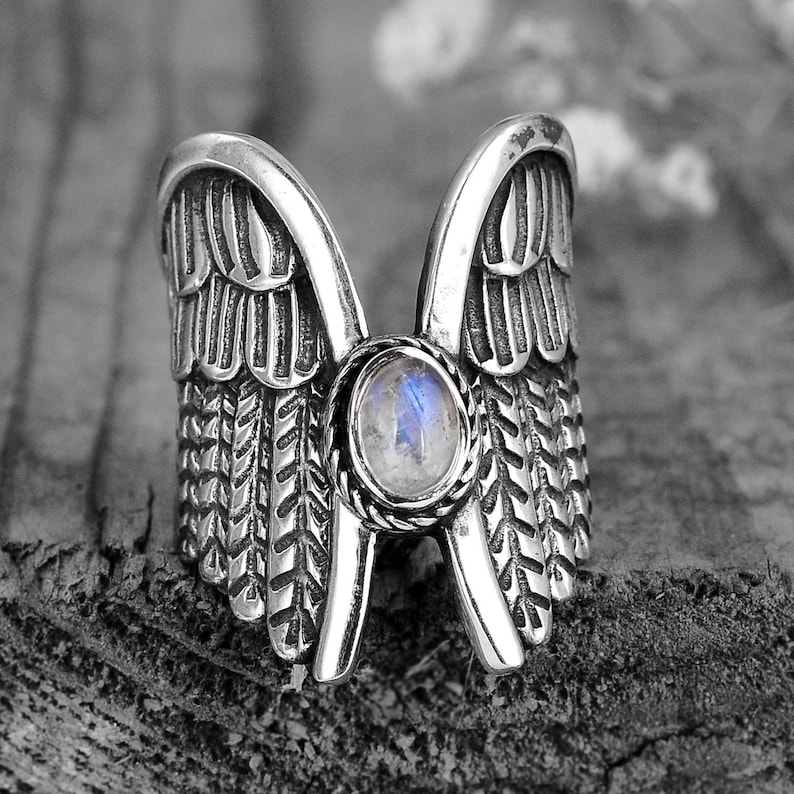 May include: A silver ring with a large, round, iridescent gemstone set in the center. The ring is shaped like a pair of wings.
