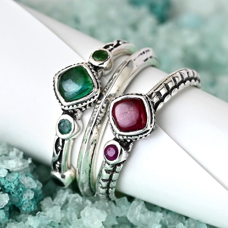May include: Three silver rings with green and red gemstones. The rings are stacked on top of each other and have intricate designs.