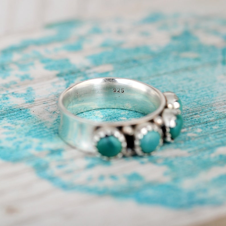 May include: A silver ring with turquoise stones set in a band. The ring is marked "925" on the inside.