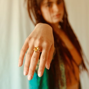 May include: A close-up of a hand wearing a silver ring with a teardrop-shaped yellow gemstone. The ring is on the index finger.