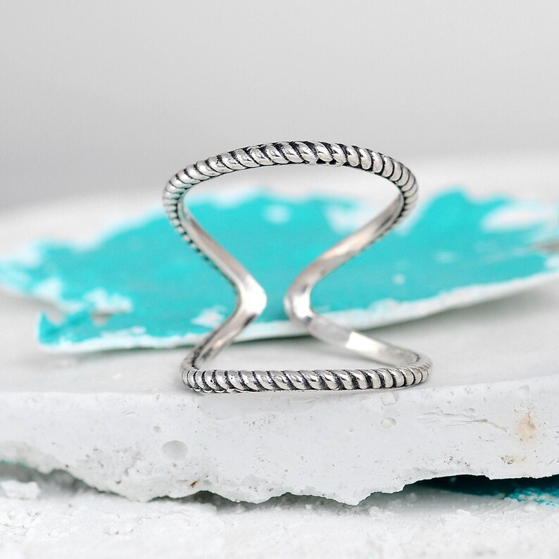 May include: A silver ring with a twisted rope design. The ring is open and has a simple, minimalist style.