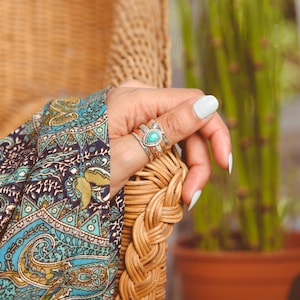 May include: A silver ring with a turquoise stone set in a teardrop shape. The ring is stacked with two other silver bands.