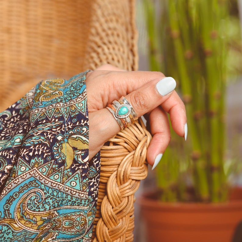 May include: A silver ring with a turquoise stone set in a teardrop shape. The ring is stacked with two other silver bands.