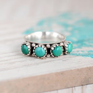 May include: A silver ring with three turquoise stones set in a scalloped design.
