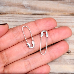 K&ouml;nnte beinhalten: Ein Paar silberne Sicherheitsnadel-Ohrringe. Die Ohrringe sind schlicht und minimalistisch und w&auml;ren ein tolles Geschenk f&uuml;r einen Freund oder eine geliebte Person.