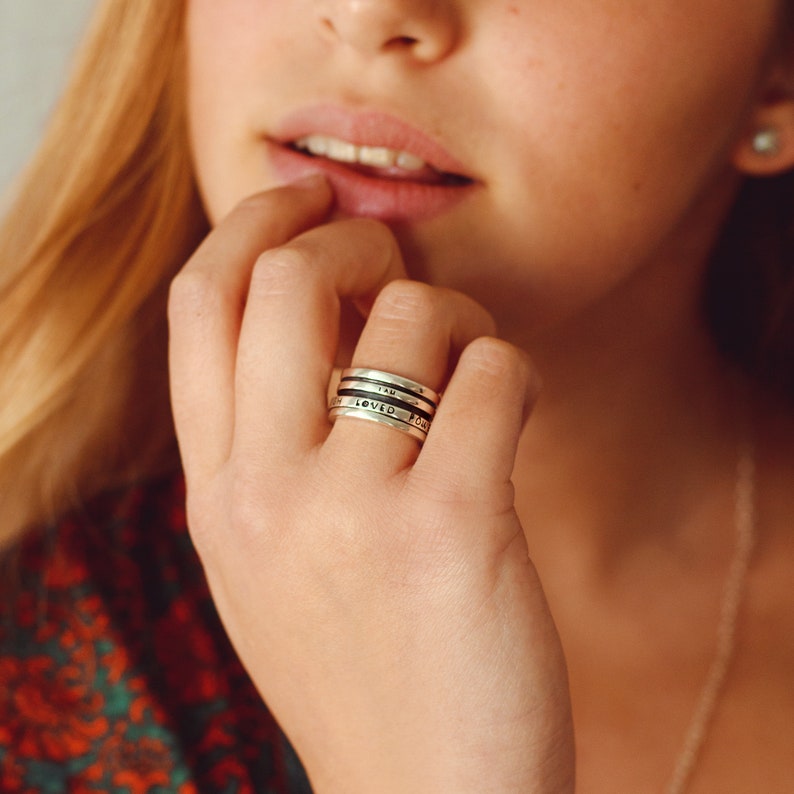May include: A close-up of a hand wearing a silver ring with the words "I am loved" engraved on it.