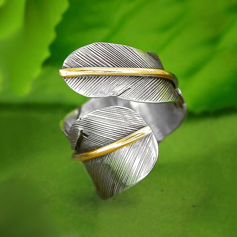May include: A silver ring with a gold accent in the shape of two overlapping feathers.