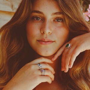 May include: A woman wearing several silver rings with green and red gemstones. The rings are on her fingers and are visible in the image.