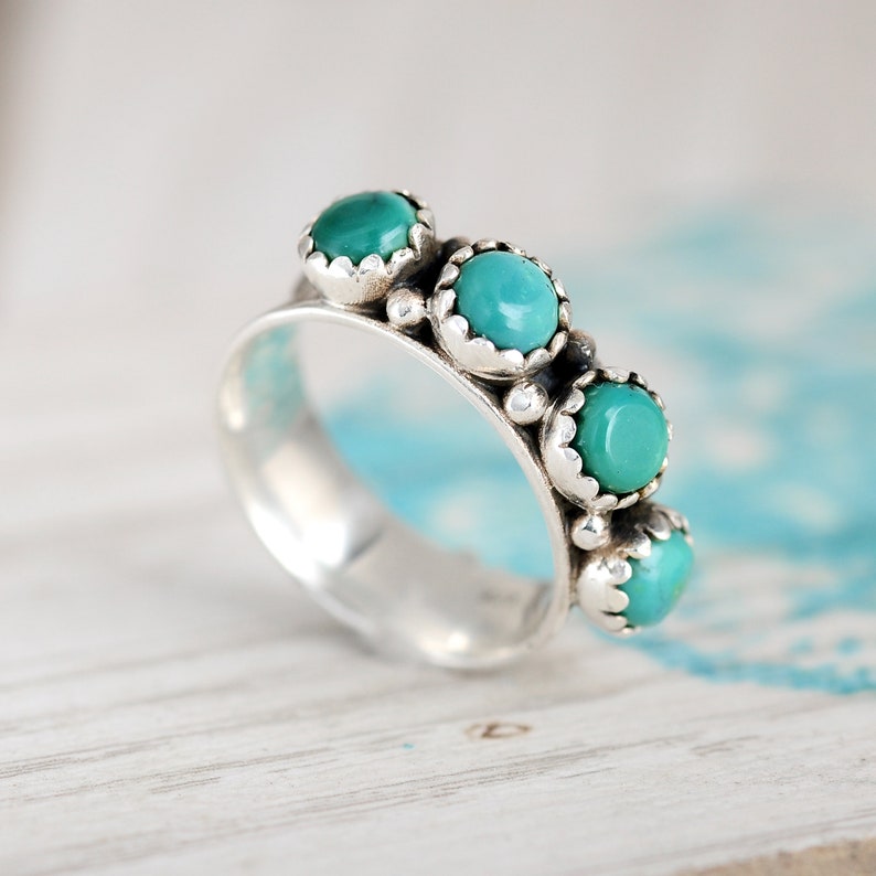 May include: A silver ring with five turquoise stones set in a scalloped design.