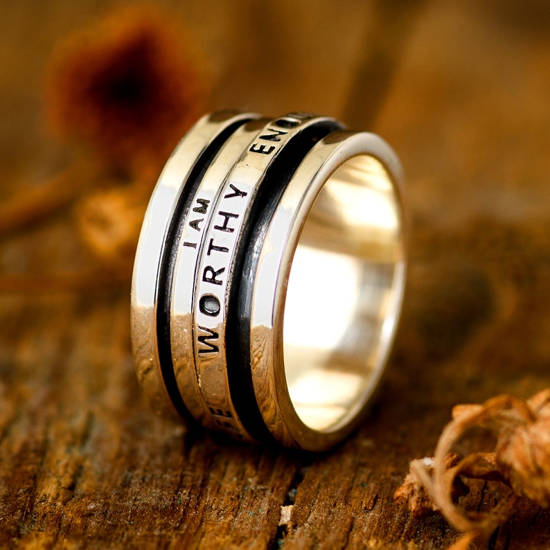 May include: A silver ring with a black band and the words "I AM WORTHY ENOUGH" engraved on it.