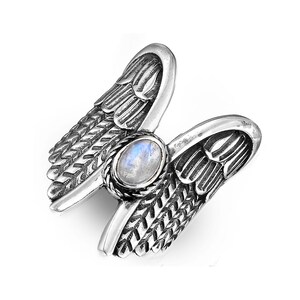 May include: A silver ring with a moonstone set in the center, surrounded by two detailed angel wings.