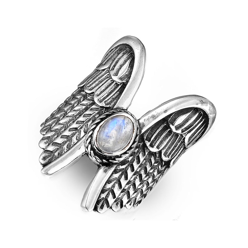 May include: A silver ring with a moonstone set in the center, surrounded by two detailed angel wings.