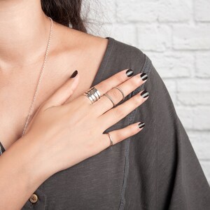 May include: A hand with black nail polish is wearing several silver rings. The hand is resting on a gray shirt.