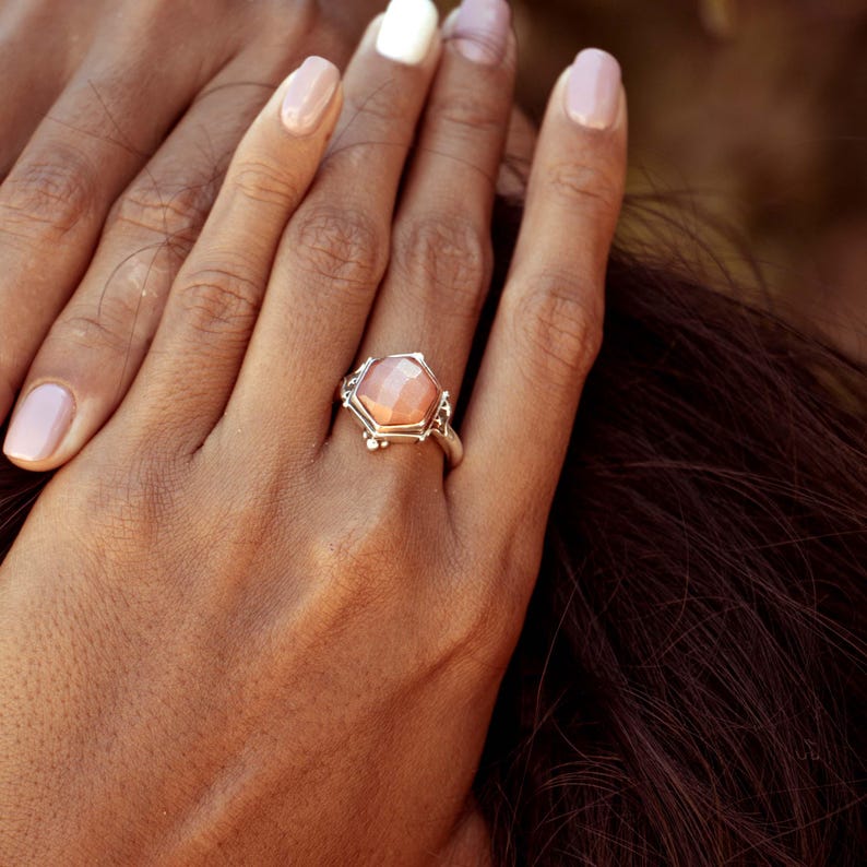 Op de afbeelding: Een zilveren ring met een zeshoekige roze edelsteen gezet in een delicaat zilveren frame.