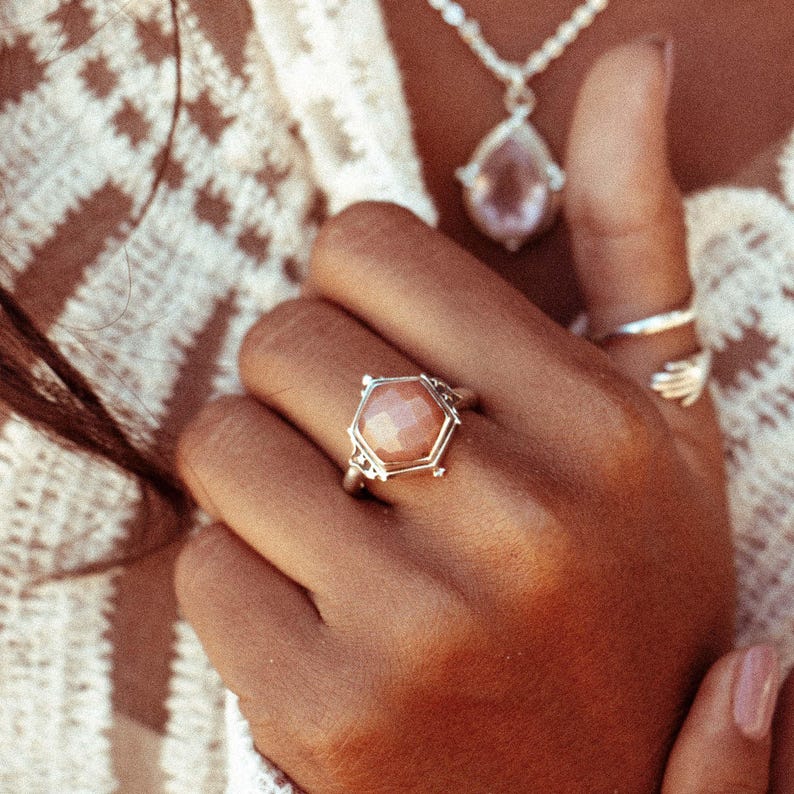 Op de afbeelding: Een zilveren ring met een zeshoekige roze edelsteen gezet in een gedetailleerd zilveren frame.