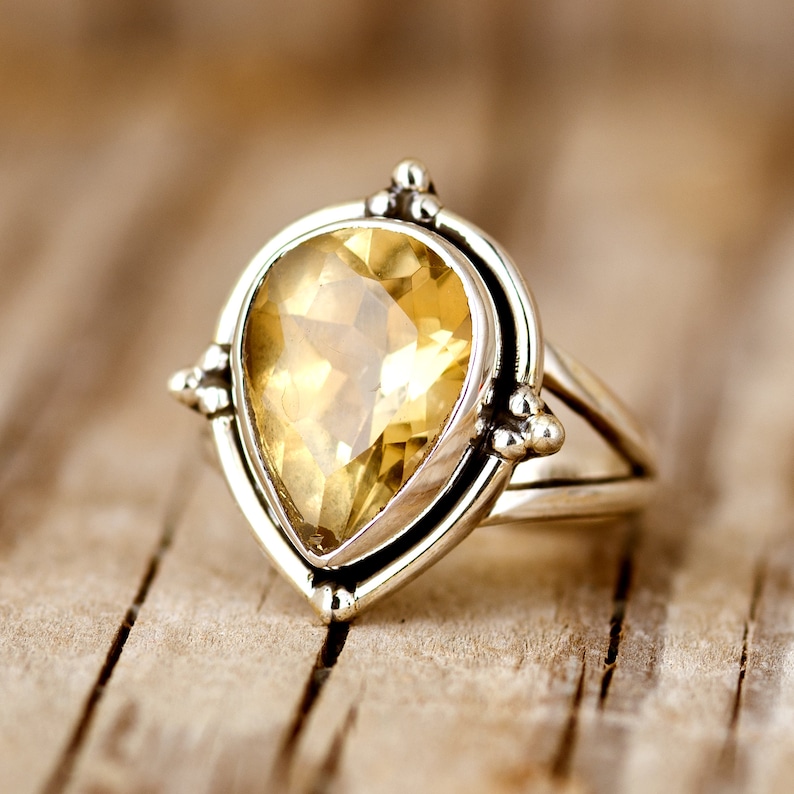 May include: A silver ring with a teardrop-shaped yellow gemstone set in a silver bezel. The ring has a delicate design with small silver accents.