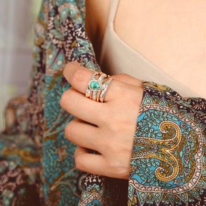 May include: A silver ring with a teardrop-shaped turquoise gemstone set in the center. The ring is stacked with other silver and gold bands.