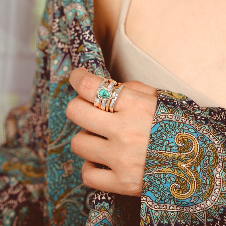 May include: A silver ring with a teardrop-shaped turquoise gemstone set in the center. The ring is stacked with other silver and gold bands.