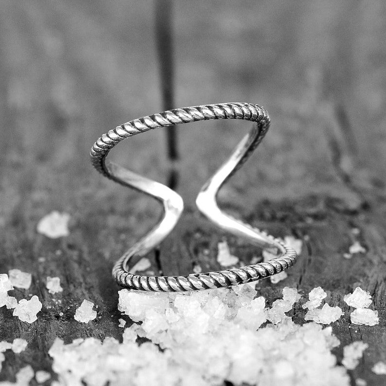 May include: A silver ring with a twisted rope design. The ring is open and has a gap in the middle.
