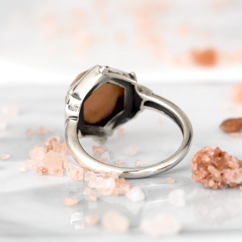 Op de afbeelding: Een zilveren ring met een zeshoekige edelsteen. De edelsteen is lichtroze.