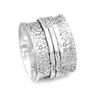 May include: A silver spinning ring with a floral design. The ring is made of three bands, each with a different texture. The top band is smooth, the middle band is hammered, and the bottom band is engraved with a floral pattern.