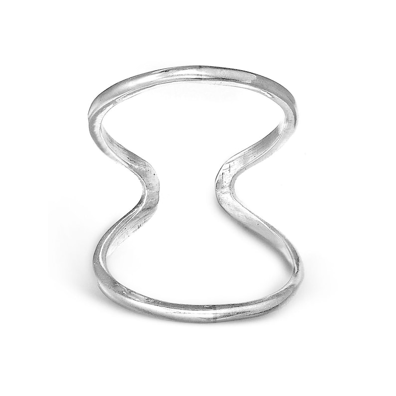 May include: A silver-colored ring with a unique double-band design. The ring features a smooth, polished finish and a distinctive open center, creating a modern and minimalist aesthetic. The ring's shape is reminiscent of an abstract figure eight.