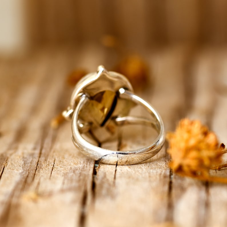 May include: A silver ring with a large, faceted gemstone set in a bezel setting. The ring is on a wooden surface.