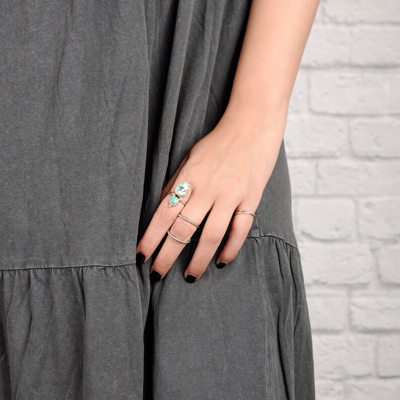 May include: A hand wearing several silver rings with turquoise and clear gemstones. The hand is wearing a gray dress.