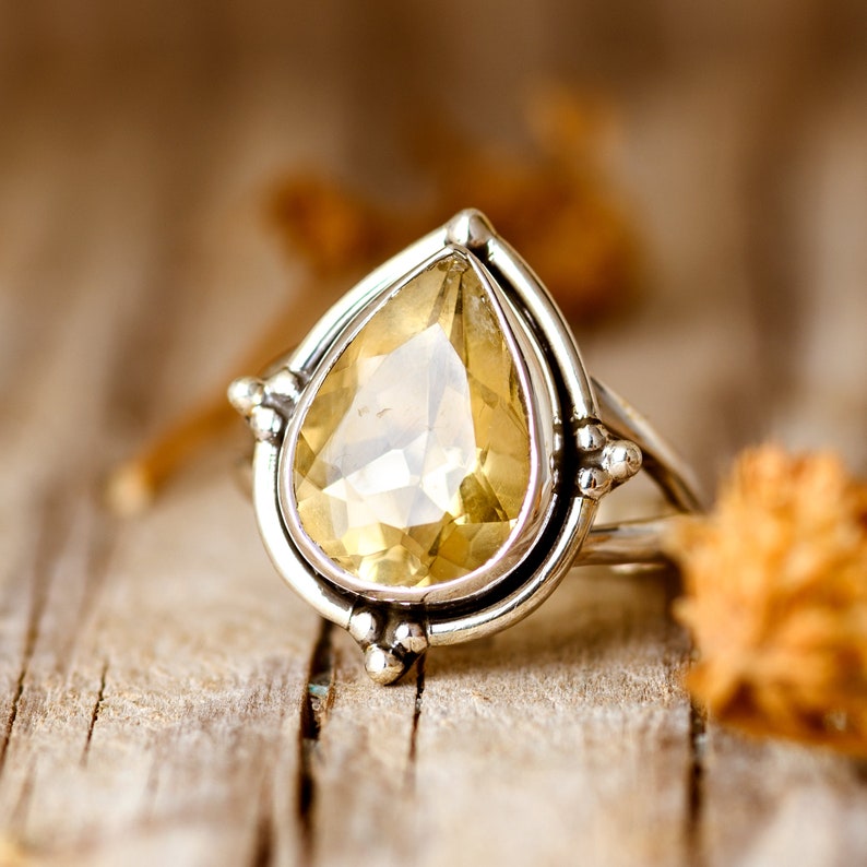May include: A silver ring with a teardrop-shaped yellow gemstone. The ring has a delicate design with small accents around the stone.