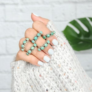 May include: A hand wearing five turquoise and silver rings. The rings are stacked on each finger and feature a row of turquoise stones.