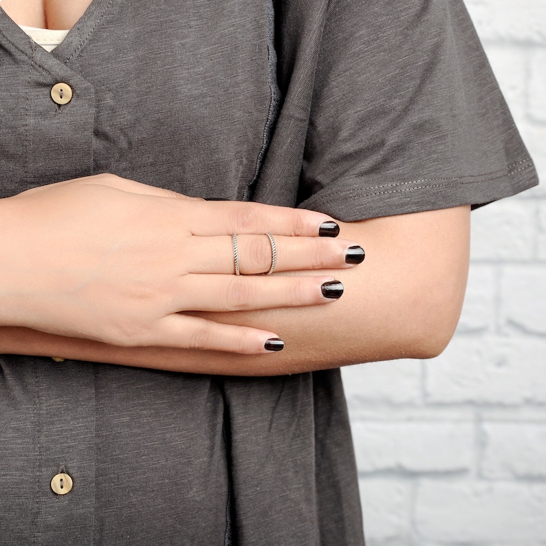 May include: A close-up of a hand wearing two thin silver rings. The hand is resting on a gray shirt. The nails are painted black.