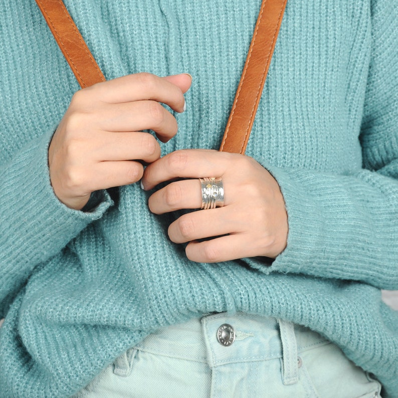 May include: A silver ring with multiple bands, each with a hammered texture. The ring has a small yellow stone set in the center.