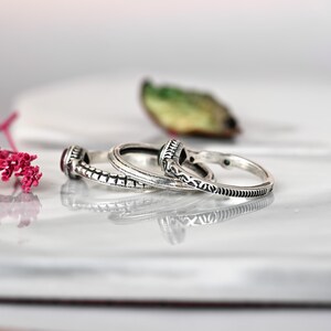 May include: Two silver rings with intricate designs. One ring features a pink gemstone, while the other has a green gemstone.