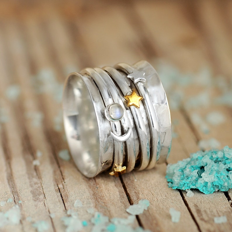 May include: A silver spinning ring with a moon and stars design. The ring has a hammered finish and features a moonstone accent.