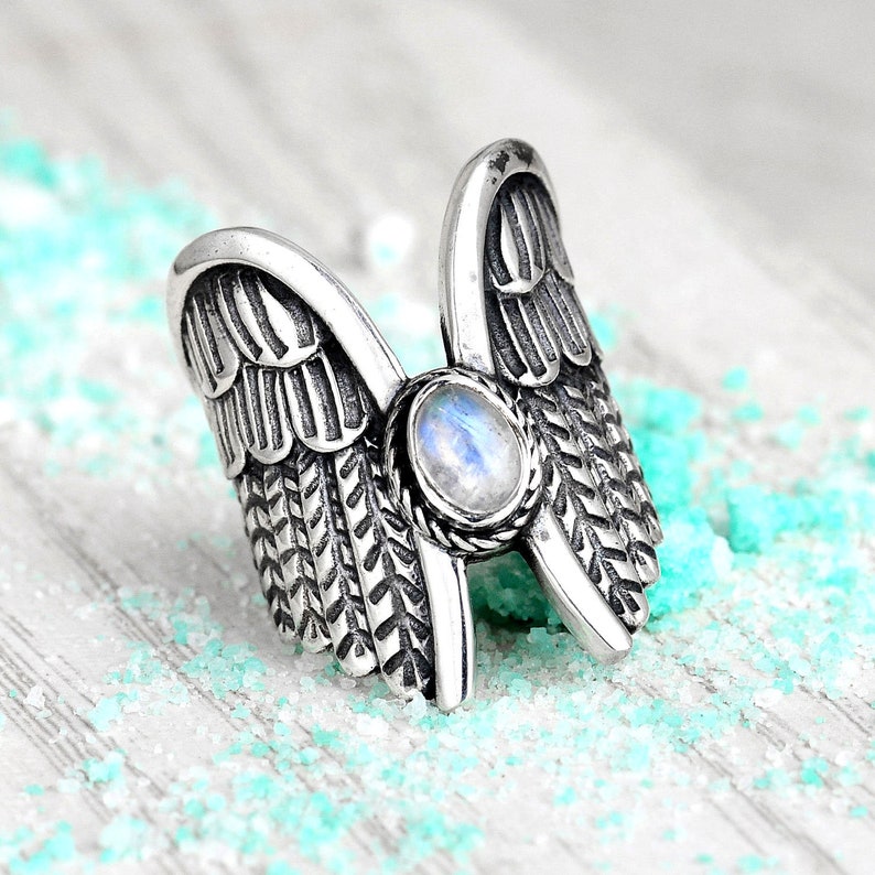 May include: Silver ring with a moonstone set in a detailed design of two wings.