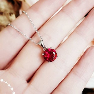 May include: A silver chain necklace with a red gemstone pendant. The pendant is a round, faceted stone set in a silver setting.